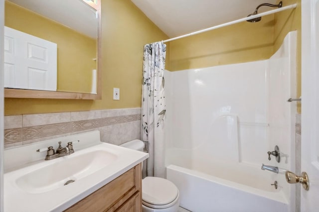 bathroom featuring toilet, a wainscoted wall, shower / bath combo with shower curtain, vanity, and tile walls