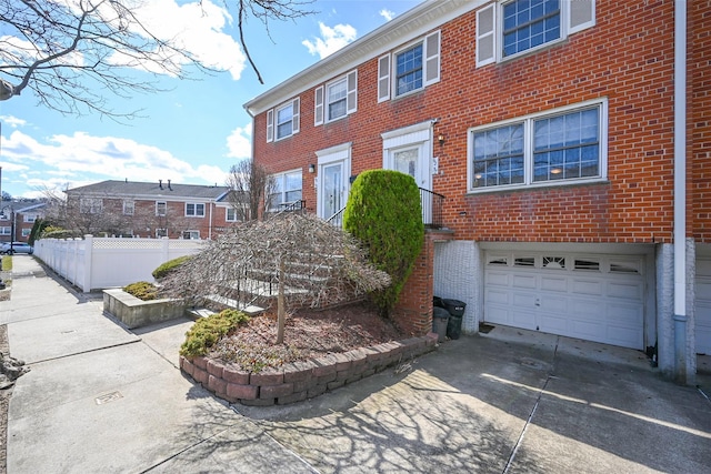 view of front of property featuring fence, a residential view, concrete driveway, a garage, and brick siding