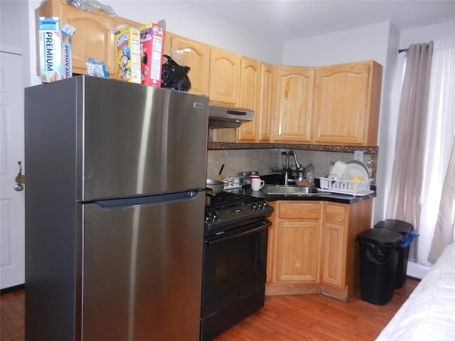 kitchen featuring freestanding refrigerator, light brown cabinets, black gas stove, a sink, and under cabinet range hood