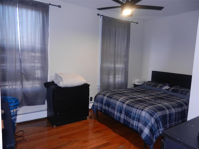 bedroom featuring a ceiling fan, baseboard heating, and wood finished floors