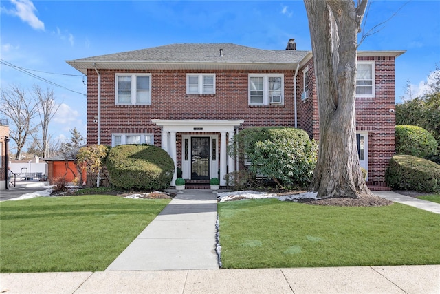 view of front of house featuring a shingled roof, a front yard, brick siding, and a chimney