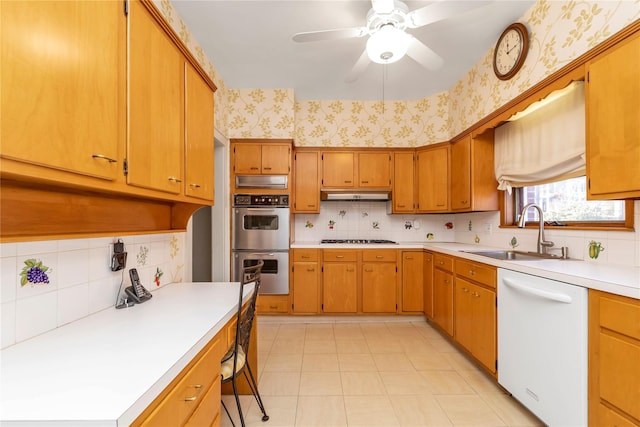 kitchen featuring stainless steel double oven, white dishwasher, a sink, and wallpapered walls