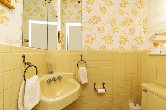 half bathroom with a wainscoted wall, a sink, toilet, and wallpapered walls