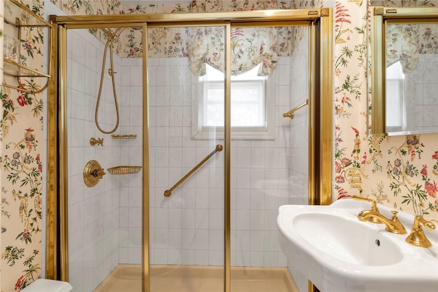 bathroom with wallpapered walls, a shower stall, and a sink