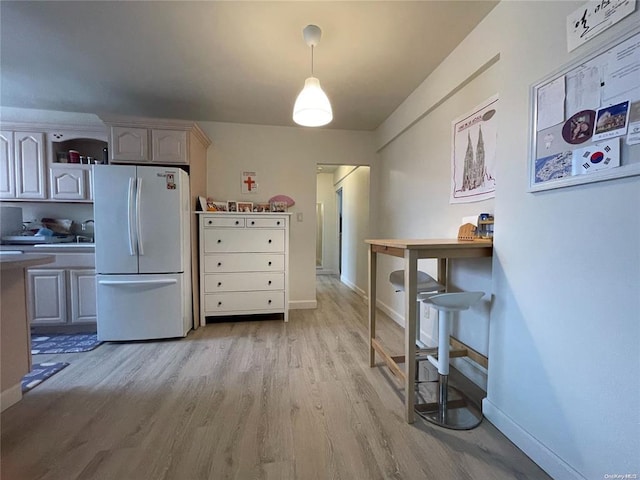 kitchen featuring light wood-style flooring, freestanding refrigerator, and baseboards