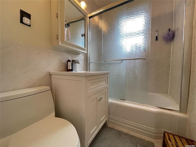 bathroom featuring shower / bath combination with glass door, vanity, toilet, and tile walls