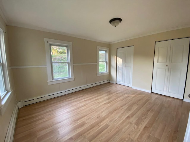 unfurnished bedroom with light wood-style flooring, crown molding, a baseboard heating unit, and multiple closets