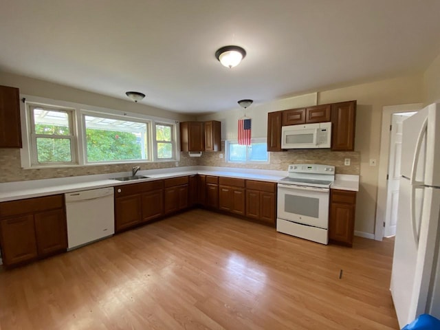 kitchen featuring white appliances, decorative backsplash, light wood finished floors, and a sink