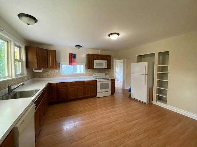 kitchen featuring white appliances, tasteful backsplash, light wood finished floors, light countertops, and a sink