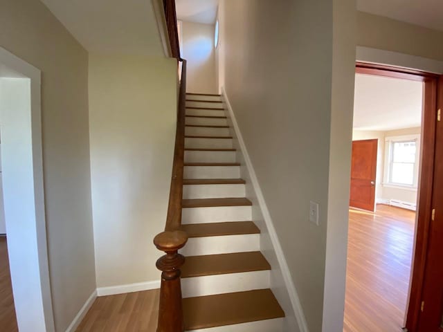 stairway with baseboard heating, wood finished floors, and baseboards