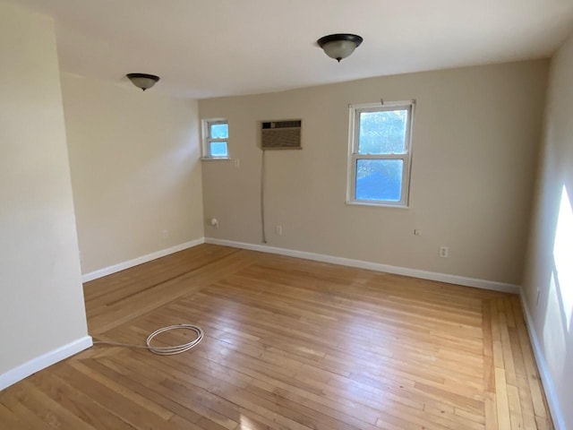 empty room featuring light wood-style floors, an AC wall unit, and baseboards