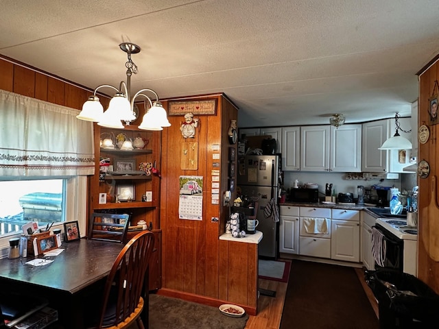 kitchen featuring a chandelier, wood walls, freestanding refrigerator, dark countertops, and white electric range oven