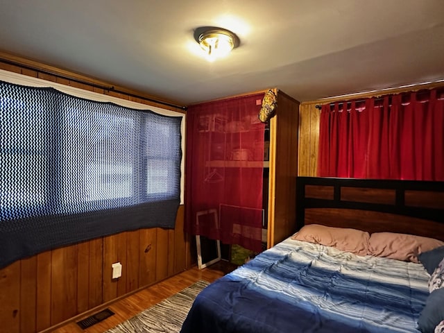 bedroom featuring wood finished floors, visible vents, and wooden walls