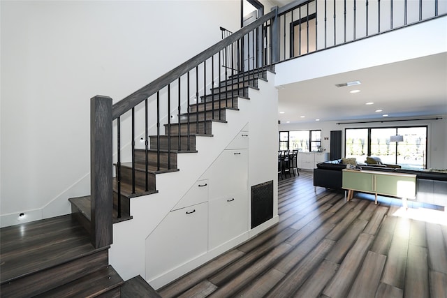 stairway featuring visible vents, wood finished floors, recessed lighting, a high ceiling, and baseboards