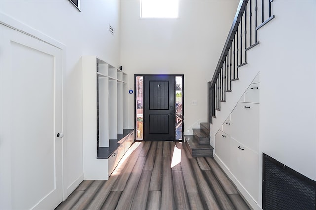 foyer featuring visible vents, wood finished floors, baseboards, a towering ceiling, and stairs