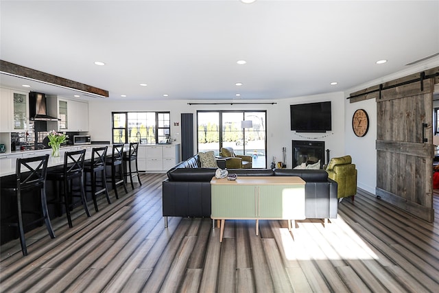 living room featuring a glass covered fireplace, recessed lighting, a barn door, and wood finished floors