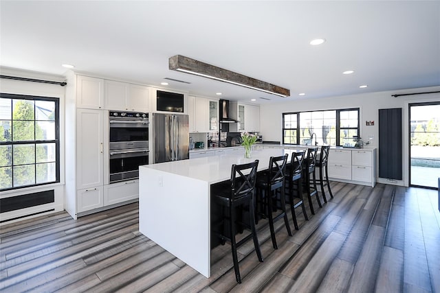 kitchen with a wealth of natural light, wall chimney range hood, appliances with stainless steel finishes, white cabinets, and light countertops