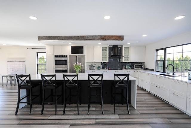 kitchen with a large island, white cabinets, stainless steel appliances, wall chimney exhaust hood, and a sink