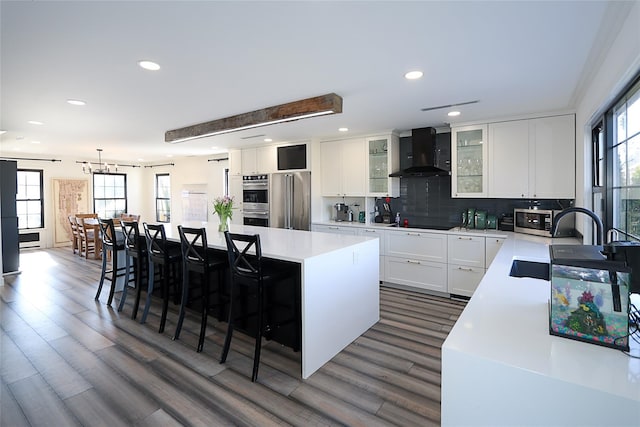 kitchen featuring a sink, a center island, appliances with stainless steel finishes, wall chimney exhaust hood, and light countertops