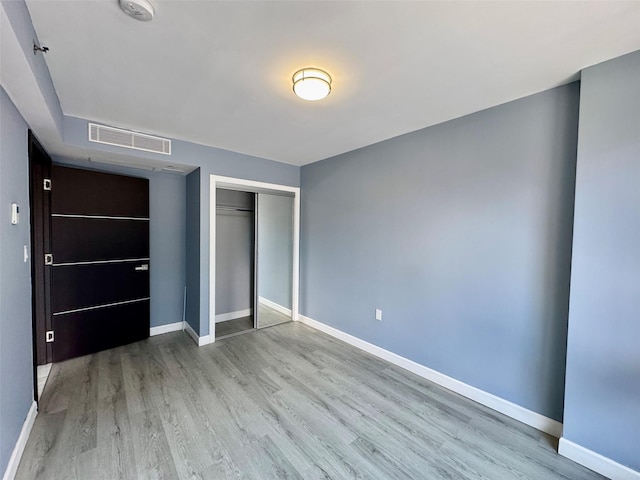 unfurnished bedroom with a closet, wood finished floors, visible vents, and baseboards