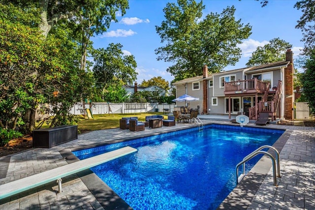 view of pool featuring stairway, fence, a deck, a patio area, and a diving board