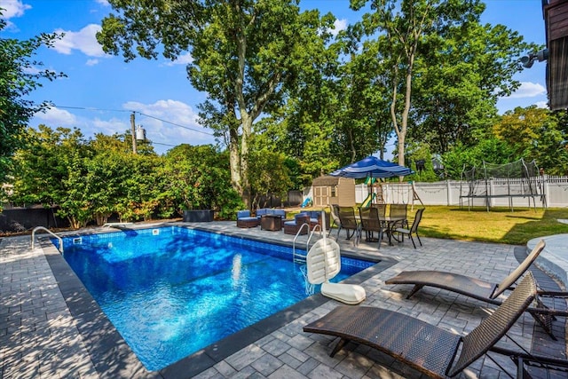 view of pool featuring a trampoline, an outbuilding, a fenced backyard, and a patio