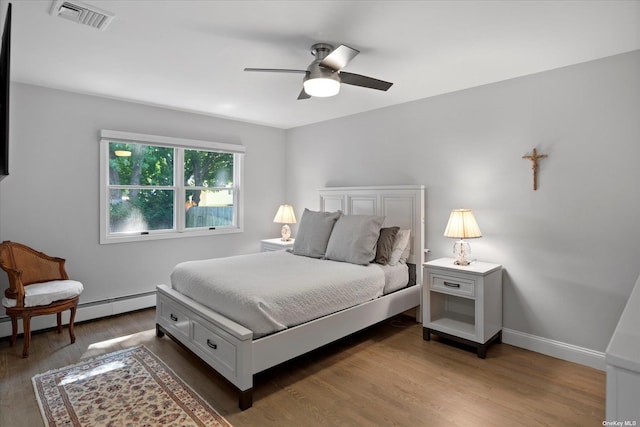 bedroom with a baseboard radiator, visible vents, ceiling fan, wood finished floors, and baseboards