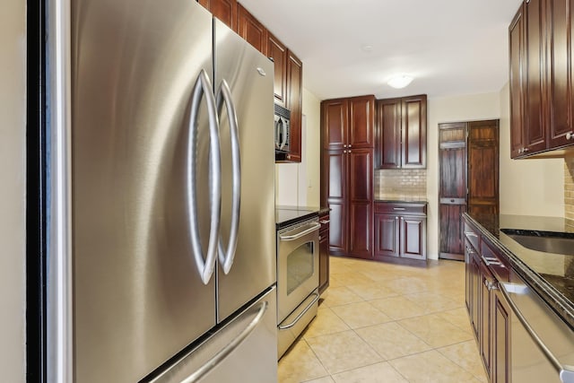 kitchen featuring backsplash, light tile patterned floors, dark stone countertops, appliances with stainless steel finishes, and reddish brown cabinets