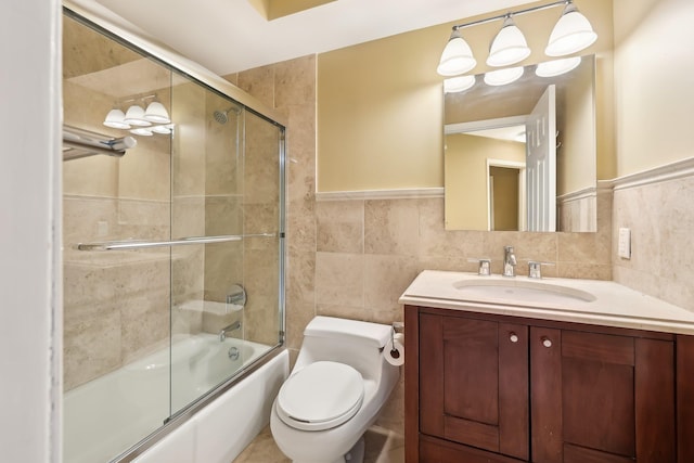 bathroom featuring toilet, tile walls, vanity, and shower / bath combination with glass door