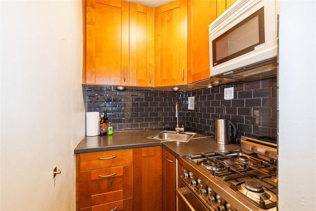 kitchen featuring stainless steel range with gas cooktop, dark countertops, decorative backsplash, white microwave, and a sink