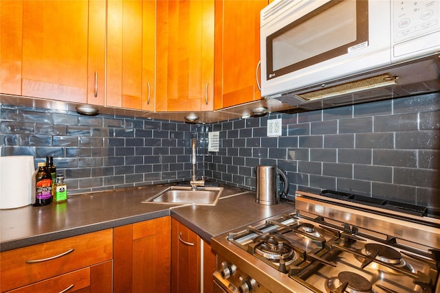 kitchen featuring white microwave, stainless steel gas range oven, a sink, backsplash, and brown cabinetry