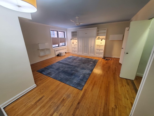 interior space featuring crown molding, light wood-style flooring, radiator heating unit, ceiling fan, and baseboards