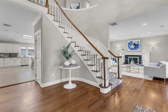 stairway with ornamental molding, visible vents, and wood finished floors