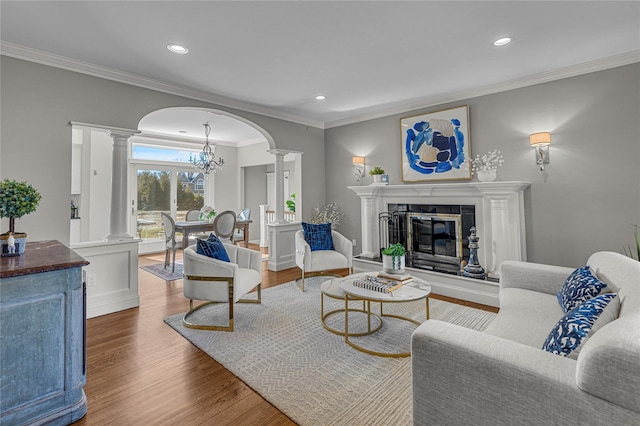 living area featuring arched walkways, wood finished floors, crown molding, ornate columns, and a high end fireplace