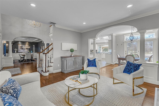 living area featuring arched walkways, wood finished floors, a notable chandelier, and ornate columns