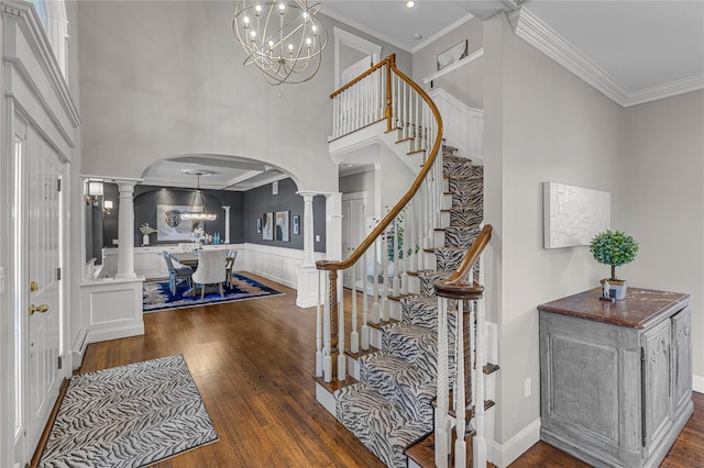 foyer entrance with arched walkways, wood finished floors, decorative columns, and crown molding