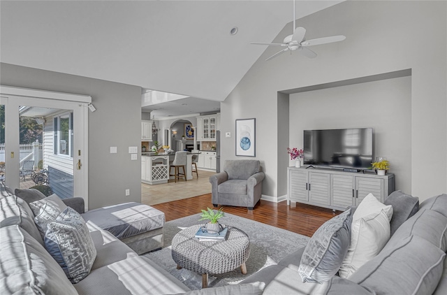 living room featuring a ceiling fan, high vaulted ceiling, baseboards, and wood finished floors