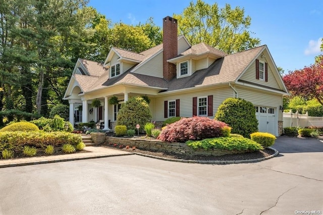 view of front facade with driveway, roof with shingles, and a chimney