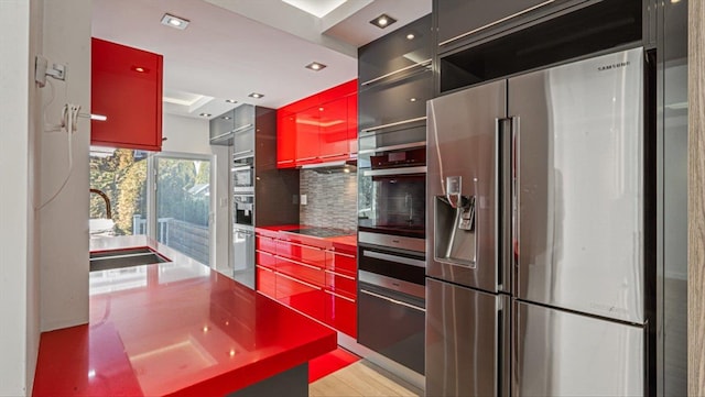 kitchen featuring a sink, appliances with stainless steel finishes, backsplash, red cabinets, and a warming drawer