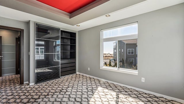 carpeted spare room with baseboards and a raised ceiling