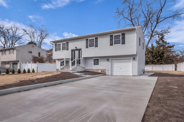 split foyer home featuring a garage, concrete driveway, and fence