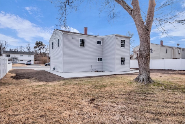 back of house featuring a lawn, a chimney, a patio, and fence