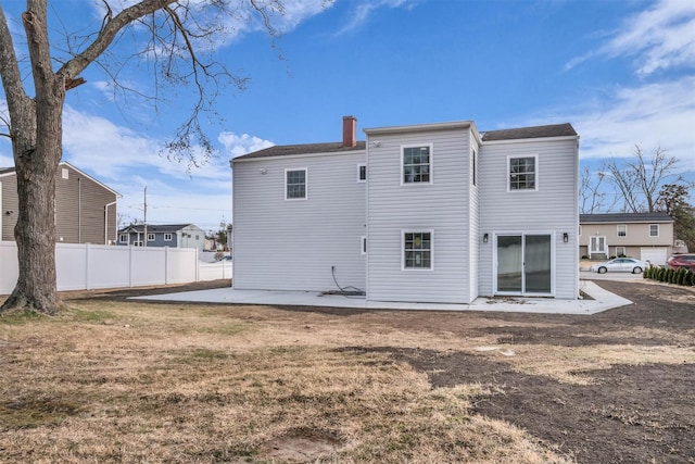 back of house featuring fence, a lawn, a chimney, and a patio area