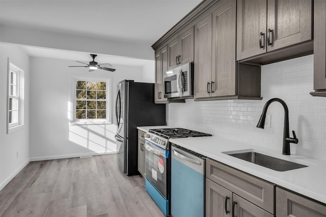 kitchen featuring light wood-style flooring, a sink, light countertops, appliances with stainless steel finishes, and tasteful backsplash