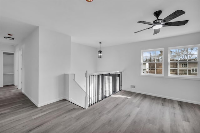 hallway featuring wood finished floors, an upstairs landing, visible vents, and baseboards