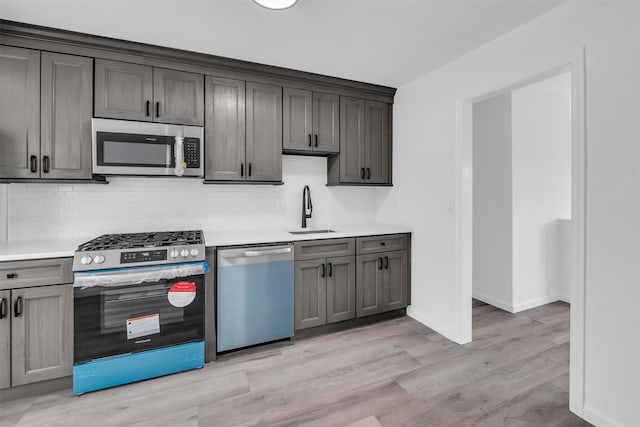 kitchen with light wood finished floors, a sink, light countertops, appliances with stainless steel finishes, and backsplash