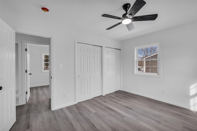 unfurnished bedroom featuring visible vents, two closets, wood finished floors, baseboards, and ceiling fan