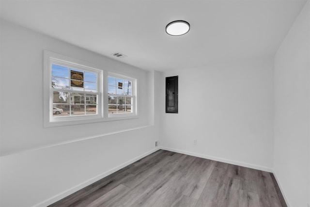 unfurnished room with electric panel, visible vents, baseboards, and wood finished floors