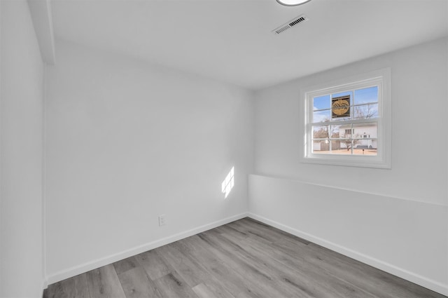 empty room featuring wood finished floors, visible vents, a wealth of natural light, and baseboards