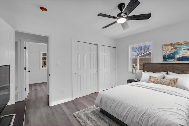 bedroom featuring visible vents, two closets, baseboards, wood finished floors, and a ceiling fan